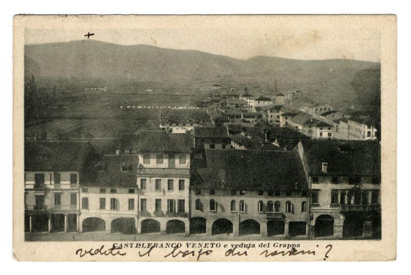 The image depicts a black and white photograph of an urban landscape, likely taken in the late 19th or early 20th century. The scene shows several rows of European-style buildings with multiple stories and features such as gabled roofs, arched windows, and balconies.

In the foreground, there is a prominent building labeled "Castelbano Veneto e veduta del Grappa," which suggests that this location may be Castelbariano in Venice or related to Grappa, an Italian wine. The handwriting on the photo appears to read something like "vedite i baro o il re?" indicating it might have some questions about viewing bars or kings.

The middle ground shows a wide street lined with these buildings and other structures extending into the distance where more architecture is visible but less distinct due to atmospheric perspective, which gives depth perception by altering how near objects are perceived in comparison to far objects. 

In the background, rolling hills or low mountains create a natura