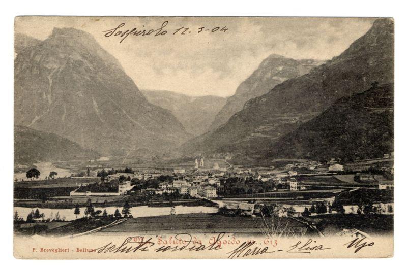 The provided photograph is a vintage postcard depicting a picturesque mountainous landscape with the village of Agordo in view. The scenery includes two prominent, rugged mountains that frame the scene on either side, leading down to what appears to be an expansive valley where the town spreads out. Within this settlement, various buildings are visible at different scales and orientations, indicative of its urban layout.

In the foreground, there's a body of water reflecting some light from above, likely a river or lake. The overall color tone is monochromatic with shades ranging from white to dark gray, suggesting that it may have been taken during midday when sunlight is bright enough to create high contrast and deep shadows in such natural settings.

Handwritten inscriptions are present on the postcard; at the top reads "Lofresiolo 12.5-04," possibly indicating a date or location associated with the photograph's creation, while additional signatures appear throughout, likely rep