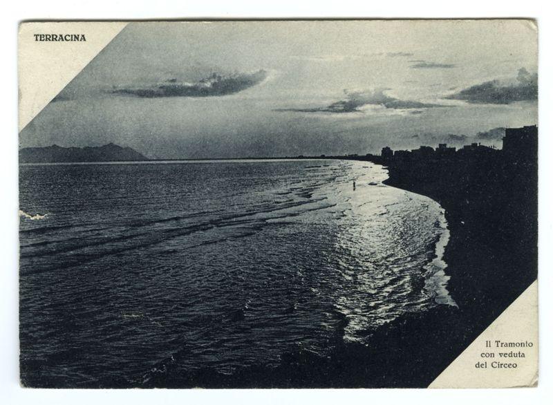 The image depicts a historical black and white postcard featuring the coastal landscape of Terracina, Italy. It shows an expansive view of the beach with gentle waves lapping against it as they recede towards the ocean's horizon. In the distance are silhouetted mountains or hills under a cloudy sky, adding depth to the scene. The right side of the postcard is bordered by buildings that seem residential and commercial structures typical for coastal towns during early 20th-century times.

In the foreground on the lower right corner, text reads "Il Tramonto con veduta del Circeo," which translates from Italian as "The Sunset with a View of Mount Circeo." The word "TERRACINA" is prominently displayed in bold at the top left side, indicating that this postcard was likely produced to promote tourism or travel interest for visitors interested in visiting Terracina.

This image captures a serene moment by the sea during sunset, emphasizing tranquility and natural beauty. It appears aged wi