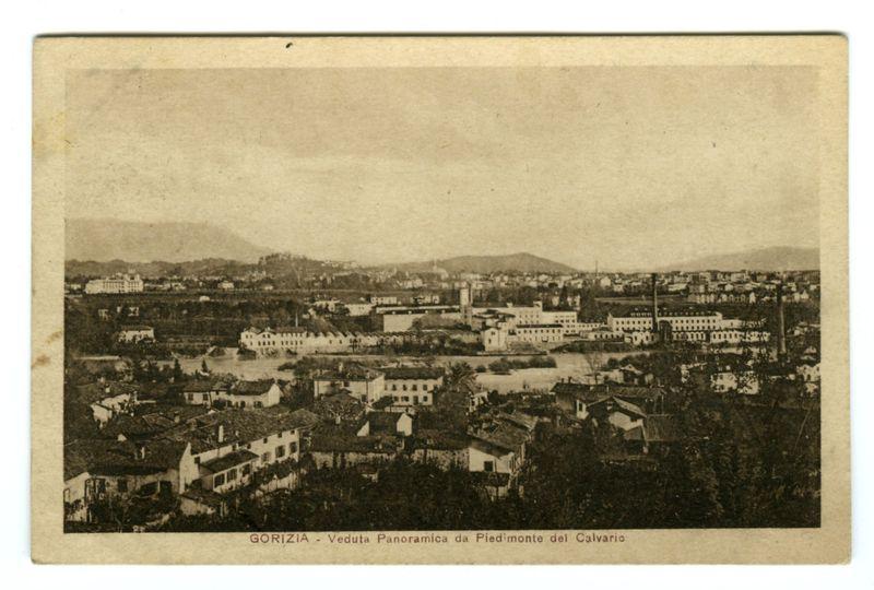 This image is a black and white vintage photograph depicting an aerial view of Gorizia, with the caption "GORIZIA - Veduta Panoramica da Piedimonte del Calvario" indicating that it shows a panoramic view from above. The town appears densely packed with various buildings, including what looks like residential houses and larger structures which could be public or industrial facilities. In the background, there is a hilly landscape leading to higher elevations where smaller clusters of buildings are visible against the horizon line.

The photograph has an aged look typical of early 20th-century postcards, with some wear around the edges indicating its considerable age and historical value. The text at the bottom suggests that this image was part of a series titled "Veduta Panoramica da Piedimonte del Calvario," which translates to "Panoramic View from Piedmonte del Calvario." This indicates that Gorizia is likely located in Italy, as Piedmonte refers to the region known for being one of