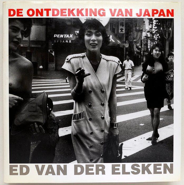 The image is a black and white photograph from an album or magazine cover titled "DE ONTDEKKING VAN JAPAN" by Ed van der Elsken. The photo depicts a busy street in Japan with pedestrians crossing the road at a zebra crossing. In the foreground, there's a woman standing on the pedestrian path dressed in a military-style dress adorned with decorative elements such as buttons and epaulettes, which could be indicative of her style or possibly represent some cultural significance related to Japanese fashion during that era.

In the background, several other individuals are visible; one person is walking away from the camera holding what appears to be a cigarette, while another woman walks in front with an exposed chest. There's also a man on the opposite side waiting to cross. The street has various signs and neon lights indicative of urban development typical for Japanese cities during that time.

The text "ED VAN DER ELSKEN" is prominently displayed at the bottom center of the image, 