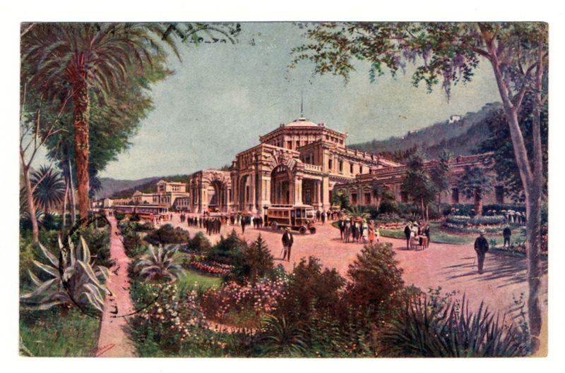The image depicts a colorful illustration of an elaborate building with classical architectural features, such as columns and arches. This appears to be the central focus of a bustling public space surrounded by lush greenery, including palm trees, shrubs, flowers, and flowering plants like agave in various shades of green and purple. The scene is lively; numerous people are seen engaging in different activities—walking along paths, conversing on benches, or strolling through what appears to be the courtyard garden area with well-maintained flower beds.

The background shows a hillside dotted with trees and possibly buildings or structures further away from the main building. A carriage pulled by horses is visible near the entrance of this grand establishment, suggesting that it may serve as an important social venue during its time. The overall impression conveyed by the image suggests an affluent setting likely to be associated with leisure activities in a European city.

In term