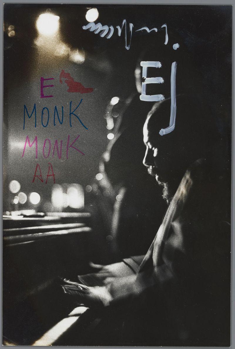 The image is a monochrome photograph with handwritten text in multiple colors. It features the silhouette of an individual who appears to be playing a piano, as indicated by their posture and what seems like keys at the lower part of the frame. The background has blurry light spots that suggest movement or out-of-focus city lights, typical of street photography from its era.

Prominently displayed in the upper left corner are three lines of text: "E MONK" with each letter colored differently—red for 'E', blue for 'MONK', and pink again for 'MONK'. To the right side, there's a large white handwritten cursive script that reads "E J". Below this individual, in smaller letters but still discernible, is another line of text: "AA".

The overall composition has an artistic feel with its use of colors to highlight specific names and the monochromatic tones creating a moody atmosphere. The photograph captures what appears to be a candid moment from jazz culture during that period, possibly 