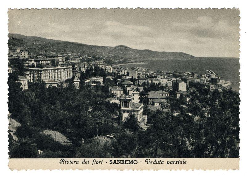 The image depicts a vintage postcard showing an aerial view of Sanremo, Italy. The scene is captured in black and white, suggesting it was taken some time ago. Prominently featured on the left side is what appears to be the Grand Hotel Presidente or another large building with classical architecture that has multiple floors and rows of windows. This structure stands out against a backdrop of rolling hills and smaller buildings spread across undulating terrain.

To the right, there are more residential houses in varying architectural styles, some with distinctive facades visible among leafy trees. The landscape below shows dense vegetation or perhaps parkland leading down towards what could be coastlines or water bodies on both sides, indicating Sanremo's coastal location.

The caption "Riviera dei fiori - SANREMO" (Ligurian Riviera) indicates that this view is of a portion of the Ligurian Riviera. The phrase suggests beauty and possibly refers to flower fields in springtime or othe