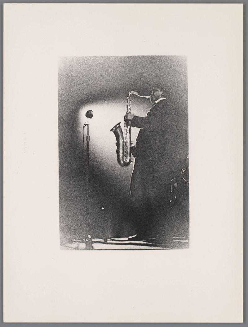 The image is a black and white photograph depicting an individual playing the saxophone. The person appears to be standing, with their body angled towards the right side of the frame, showcasing them from mid-torso upwards. They are holding a saxophone that extends vertically up in front of them, suggesting they may have just finished or paused playing it.

The lighting is dramatic and focused on the player, creating strong contrasts between light and shadow across the image. The background consists mostly of dark tones with some lighter areas at the bottom left corner which might be indicative of a stage floor or reflective surface that catches faint illumination from the performer's vicinity.

There are no discernible colors as it’s in grayscale but various shades ranging from white to black, contributing to its vintage aesthetic typical of early 20th-century photography. The person is wearing what appears to be dark clothing which blends into the darker background areas and make