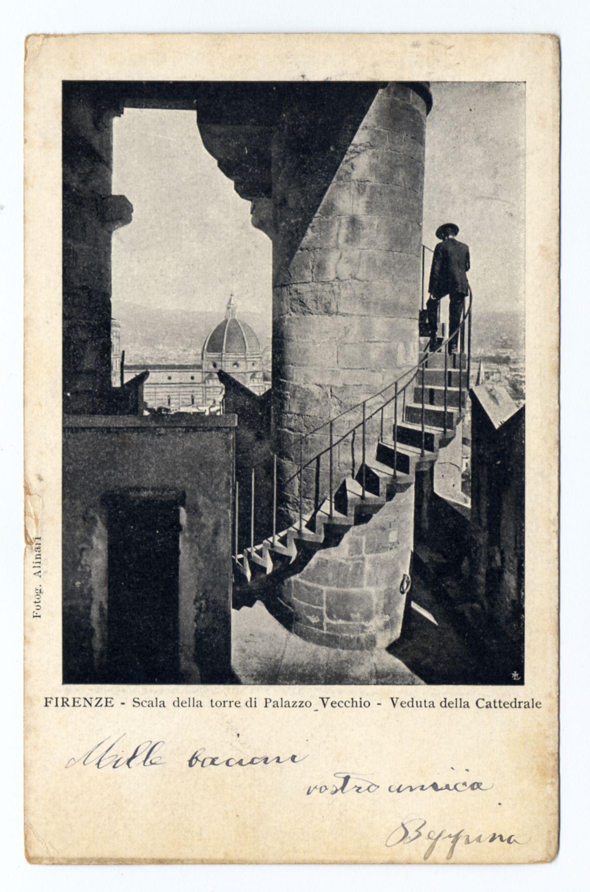 The image depicts a vintage, monochrome photograph of an architectural scene. It features a person standing on the uppermost steps of what appears to be a tower with stone balustrades leading down from it. The individual is dressed in period attire, including a hat and coat, suggesting that this photo may have been taken several decades ago.

In the background through the archway are expansive views of Florence's skyline, notably featuring the dome of Santa Maria del Fiore (The Duomo), identifiable by its distinctive Renaissance architecture with an octagonal base leading to a round drum above which sits a large spire. The presence of another prominent domed building in the distance suggests additional historical significance.

This view is from within Palazzo Vecchio, one of Florence's most iconic buildings, and it seems like the viewer might be on its tower given that "Scala della torre di Palazzo Vecchio" indicates an ascent to this historic site. The bottom section has handwrit