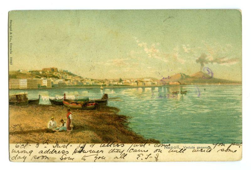 The postcard features a serene coastal scene with clear skies and calm waters. In the foreground, on what appears to be sand or a shoreline, there are four figures: three seated adults in white clothing and one child wearing red; they seem relaxed, possibly engaging in conversation or simply enjoying the view. Two boats rest idle near them, hinting at local maritime activities.

The middle ground shows gentle waves lapping against the shore and two more boats closer to a rocky outcrop with vegetation. In the background lies an urban landscape along a sloping hillside dotted with buildings indicative of a coastal town or city. A prominent feature is Vesuvius volcano in the distance, billowing smoke into the sky which contrasts significantly with the otherwise peaceful setting.

The water reflects hues ranging from green to blue and hints at marine life through slight ripples on its surface. The bottom right corner contains handwritten text that provides personal context: a date (6th