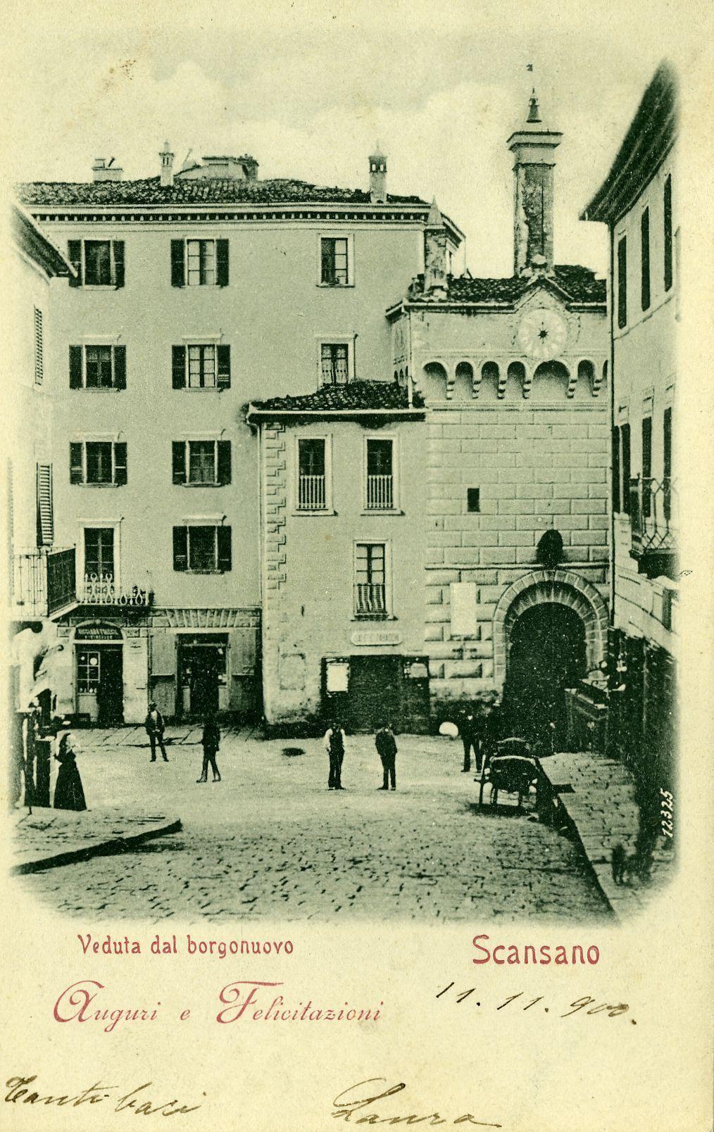 The image shows a vintage postcard depicting an old European town scene, likely from the early 20th century. The architectural style suggests it could be Italian. In the foreground is a cobblestone square with several figures dressed in period clothing, suggesting daily life and activity of that era. A prominent clock tower structure stands to the right, with arches above its main entrance and a smaller rectangular window on an upper level.

In the background are buildings featuring shuttered windows and balconies typical of European urban architecture from this time period. The sky is overcast or sepia-toned in color due to the age of the photograph. On top of each building, there appears to be what might resemble antennas or small architectural decorations. A notable feature includes a handwritten dedication at the bottom left corner that reads "Veduta dal borgonuovo" and mentions names possibly related to photography.

The text on the postcard in cursive script states "Auguri e 