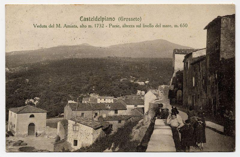 The image is a sepia-toned historical photograph depicting an old village scene, likely from the late 19th to early 20th century. The text on top of the photo reads "Casteldelpiano (Grosseto)" indicating that this place is located in Grosseto province. Below it, additional information states "Veduta del M. Amiata, alto m. 1732 - Paese, altezza sul livello del mare, m.650," which translates to a view of Mount Amiata at an altitude of 1,732 meters and the village's elevation above sea level being approximately 650 meters.

In the photograph, we see several individuals standing or walking along what appears to be a narrow road within the old town. They are dressed in period-appropriate clothing suggesting this image is from that time frame. The architecture of the buildings suggests European styles with stone construction and terracotta roof tiles.

The landscape behind them features rolling hills leading up towards Mount Amiata, which provides context for their location relative to a
