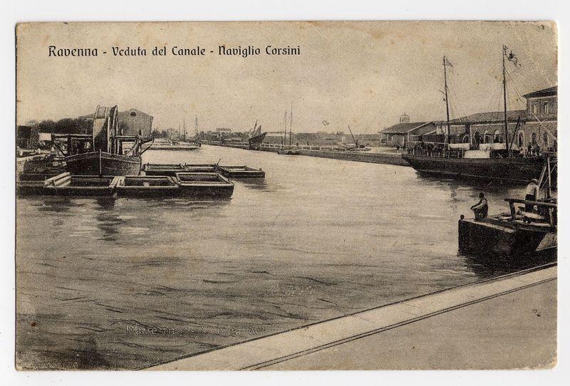The image displays a sepia-toned, vintage postcard depicting a scene at the Canal of Ravenna. In the foreground is calm water reflecting light and shadow, with several wooden boats moored along docks that jut into the canal from both sides. On one dock sits an individual who appears to be tending or resting near their boat, while on another larger vessel in the middle distance, a figure can be seen standing at the stern, possibly overseeing operations.

In the background, multiple sailing ships with prominent masts are anchored along the far side of the canal, indicating active maritime activity. The architecture lining the docks suggests European design from an earlier era, likely late 19th to early 20th century judging by style and condition.

The top portion of the postcard bears text in Italian: "Ravenna - Veduta del Canale - Navignio Corsini," which translates to Ravenna – View of the Canal - Corsini's Navigation. This suggests that the photograph may have been taken during a 