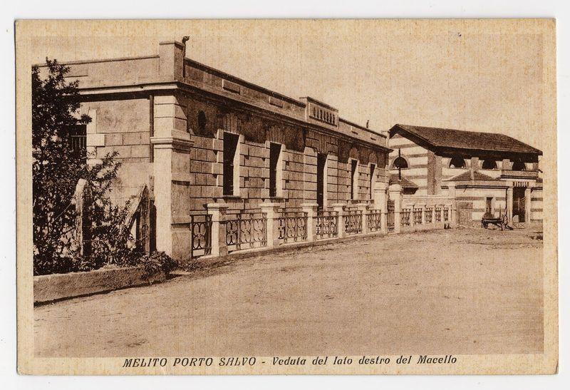 The image is a sepia-toned photograph depicting an old architectural structure identified as "MeliTo Porto Salvo - Veduta del lato destro del Macello." The building appears to be constructed with stone, featuring large rectangular blocks and detailed window frames. There's iron fencing along the perimeter of what seems like a courtyard or entrance area, and several trees are visible in front of it.

The photograph is presented on a card that has text at its bottom edge providing context for the image. The background appears to be plain without any additional details. This style suggests an early 20th-century postcard design commonly used during that period as a means of sending messages or keepsakes from travel destinations.